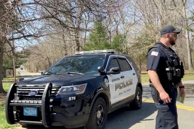 A male police officer stands beside a black and white police vehicle.