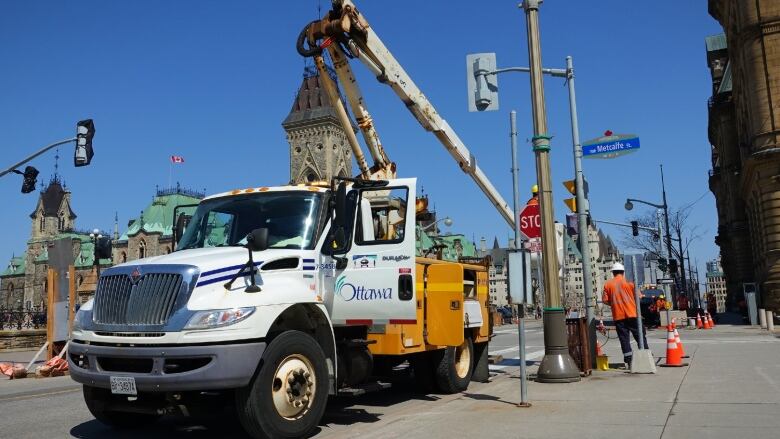 A white truck equipped with a lift so crews can do work above the ground is parked on a downtown street on a sunny day.