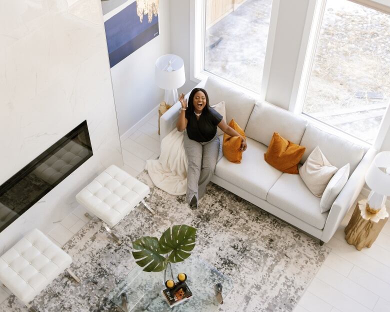 A bird's eye view of a woman sitting on a couch, kicking up her foot and smiling.