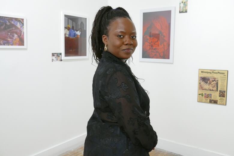 A woman stands smiling in front of several framed photos of various sizes, looking over her shoulder at the camera. 