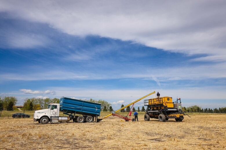 A seeder and a truck in a field, with some people monitoring the equipment.