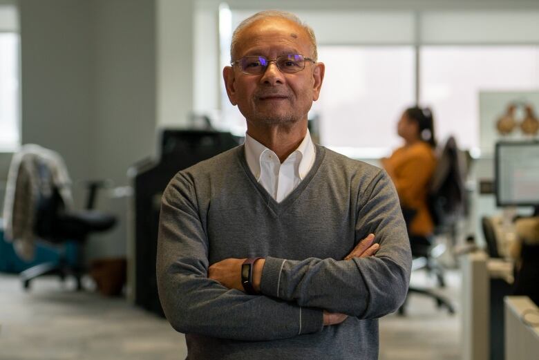 An older man stands for a portrait with his arms folded. 