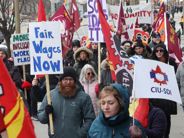 People march in a city with signs about solidarity and fair wages in early spring.