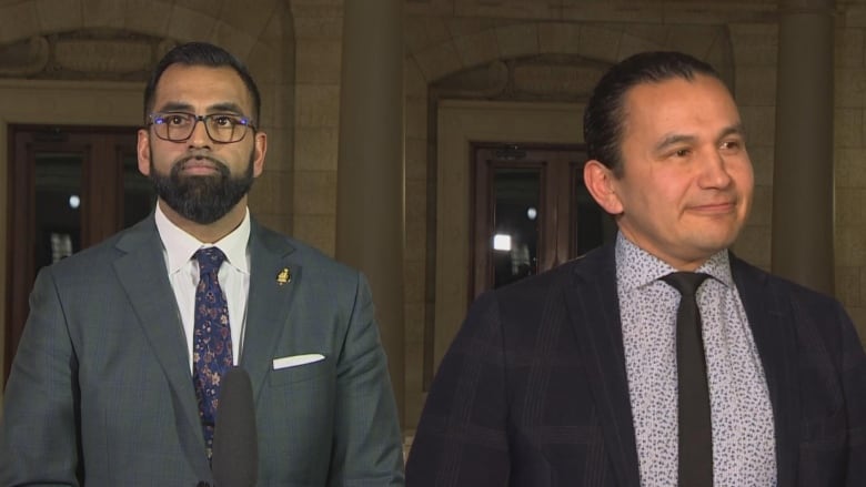 Two men wearing suits stand in a legislative building.