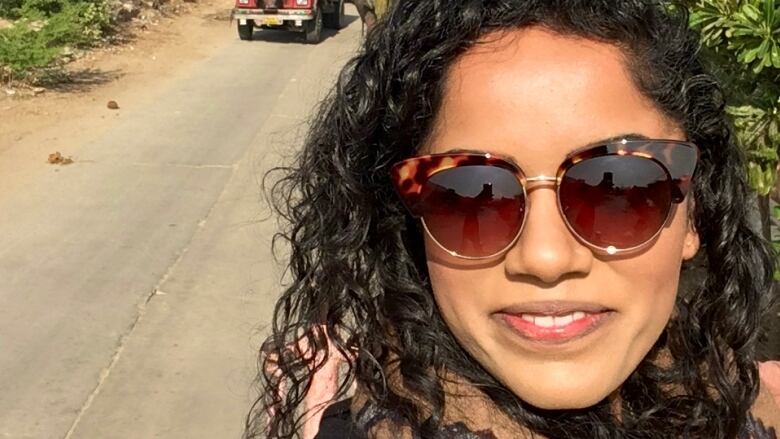 Selfie of a woman wearing sunglasses near a sunny village road.