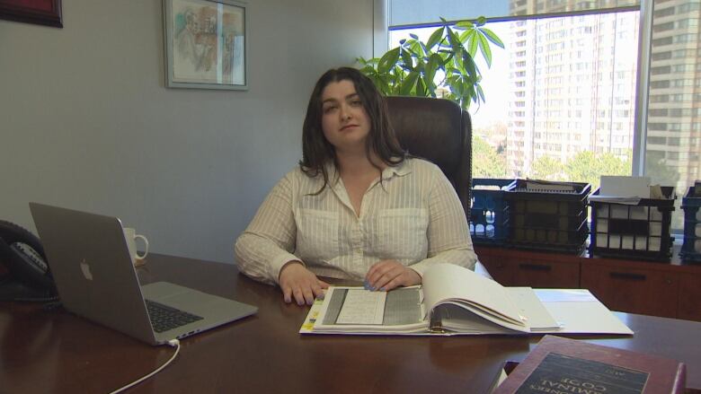 A woman in a white shirt sits at a desk with books and a computer on it.