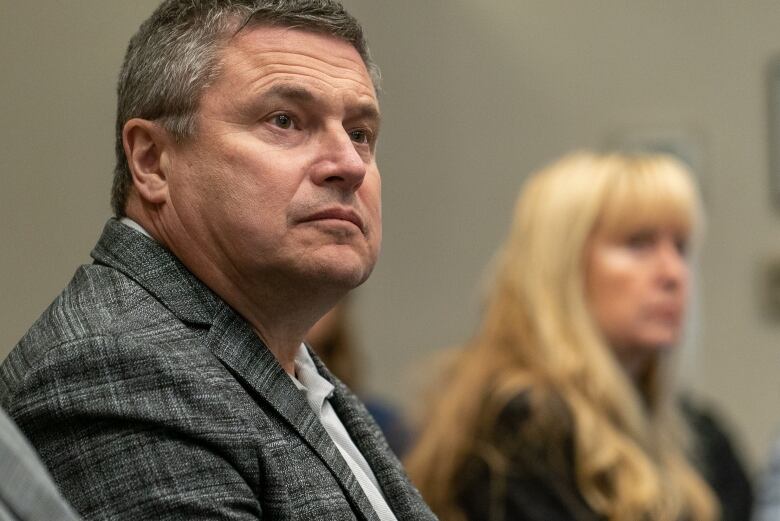 A mean wearing a white shirt and sportcoat looks off into the distance. 