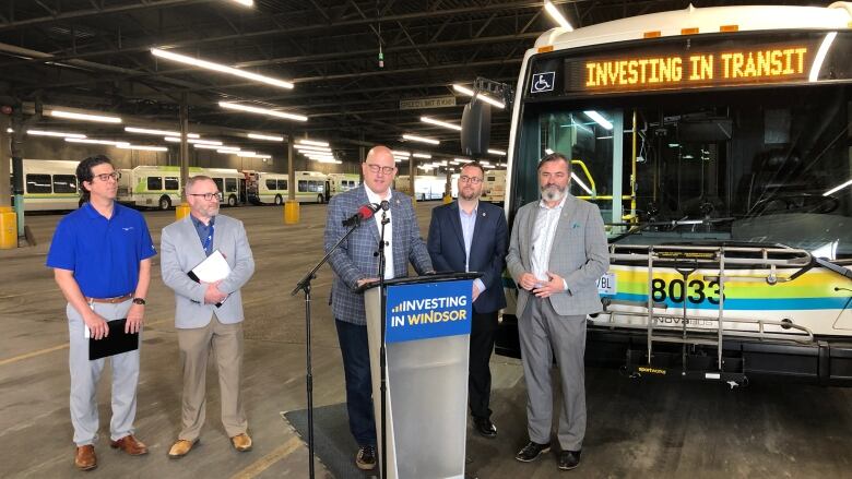 Several men stand in front of a bus that displays 