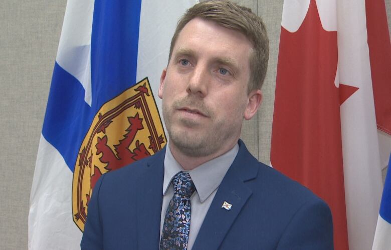 A man in a suit and tie stands in front of flags.