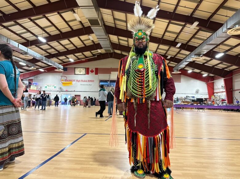 A man stands in a gym wearing a head dress and a floor-length red garment.