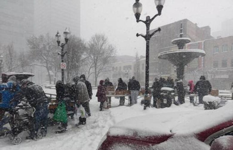 Snow filled park with people getting food. 