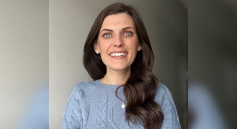 Smiling woman with long dark hair, standing with arms cross in front. 