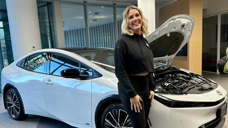 Leah Gillanders, a blonde woman wearing black, stands in front of a car with an open hood.