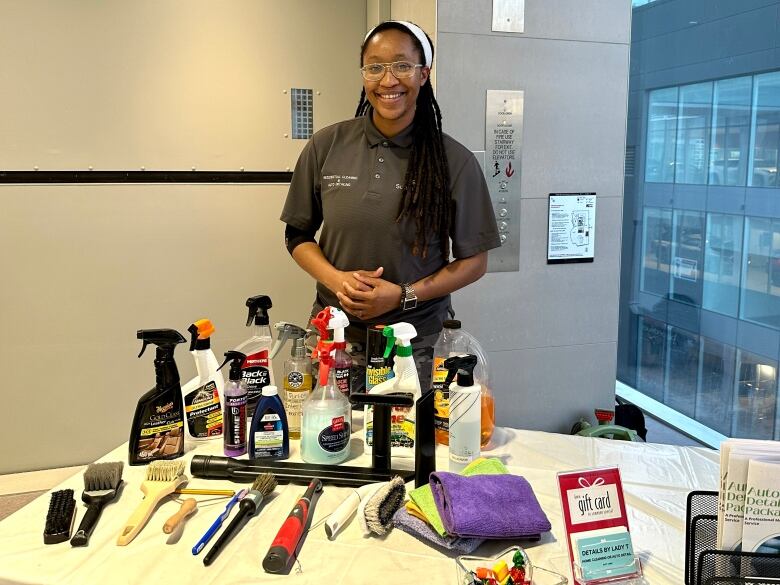 Lex Marshall, a Black woman, stands behind a desk with auto cleaning implements.