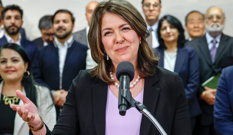 A woman stands behind a microphone and smiles. A crowd of people stands behind her.