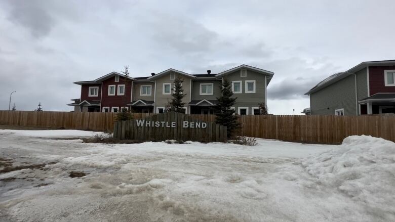 Photo shows a sign saying Whistle Bend, with houses in the back. 