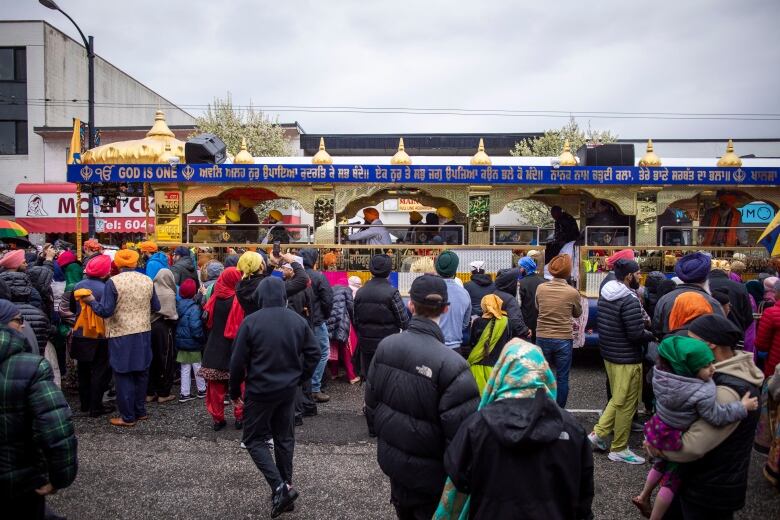 A large open-air bus adorned with gold attachments passes through a parade of people.