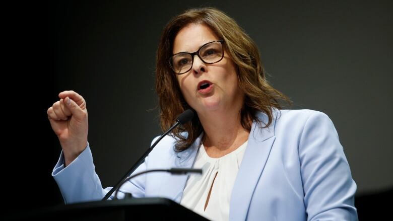 A woman in a light blue blazer speaks behind the podium. 