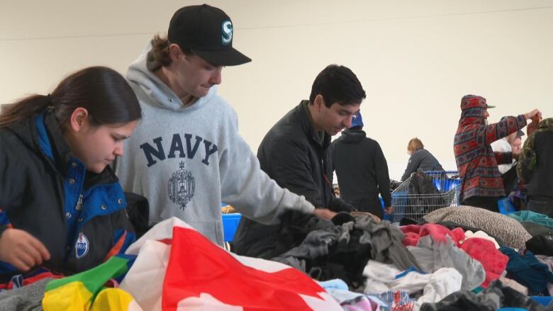 About a half dozen shoppers look through piles of clothing and fabric. One of the items appears to be a large Canadian flag. 