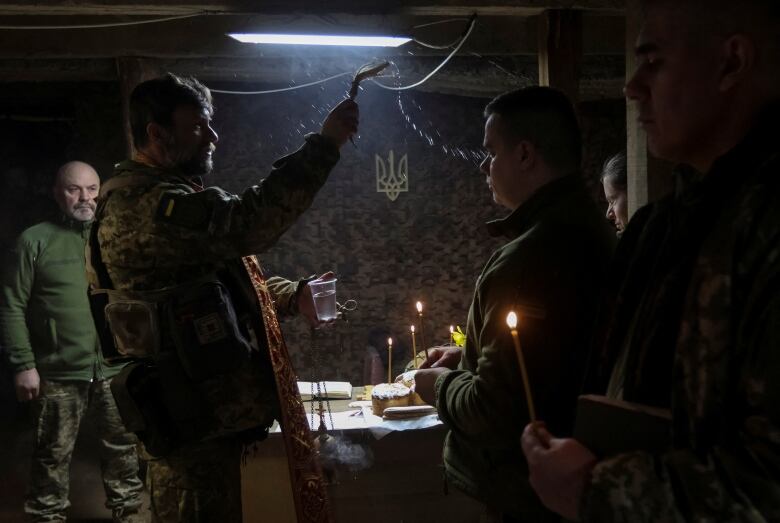 A military chaplain sprinkles holy water on service members in a dark room.