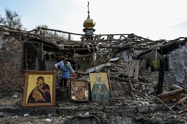 A woman collects Orthodox icons at the ruins of a church.