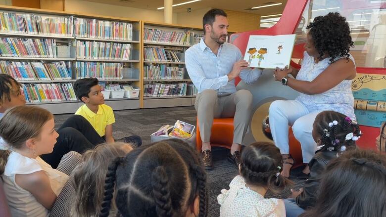 A man and a woman read a book to children at a library.