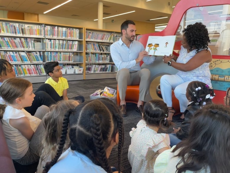 A man and a woman read a book to children at a library.