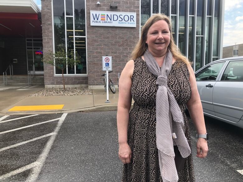 A woman wearing a black dress with brown spots and a grey scarf standing outside a library