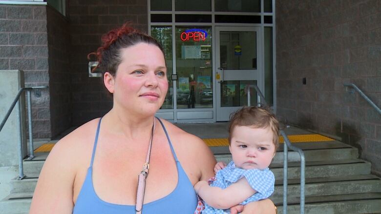 A woman wearing a blue dress with a brown purse holding her infant daughter