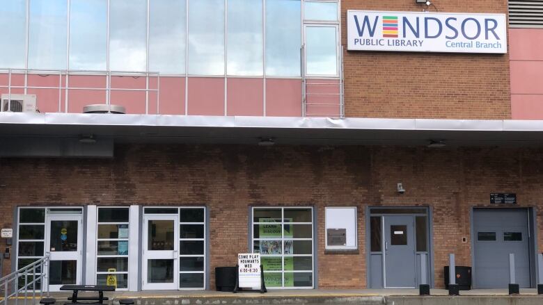 The outside of a library located in a downtown area with a sign outside