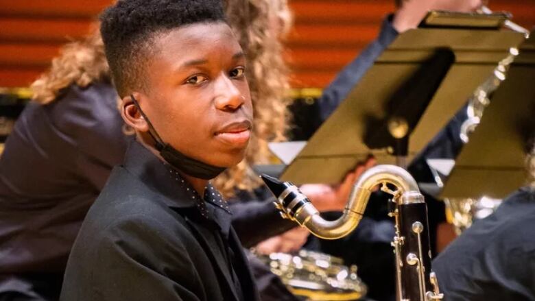 Black teen holds a saxophone during a concert.