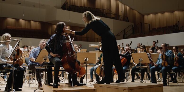 Still frame from the film Sophie Tr. Conductor Cate Blanchett touches the face of  cellist Sophie Kaur with members of their orchestra in the background.