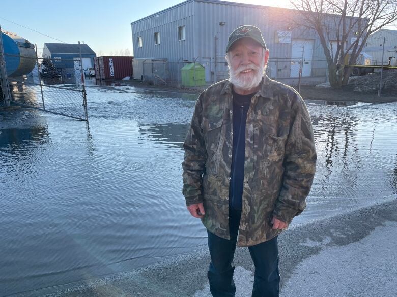 A man stands in front of a flooded parking lot next to a building.