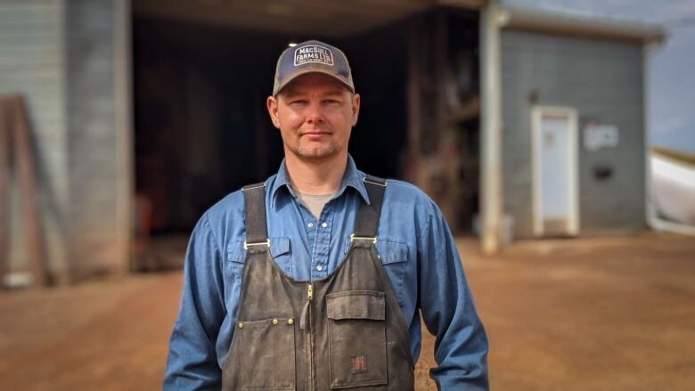 A farmer wearing overalls stands in front of his warehouse 