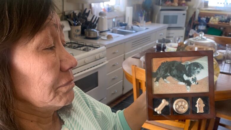 A woman holds up a photo of a black and white dog. 