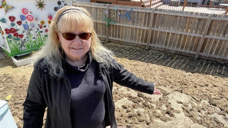 A woman in sunglasses stands outside by a shed.