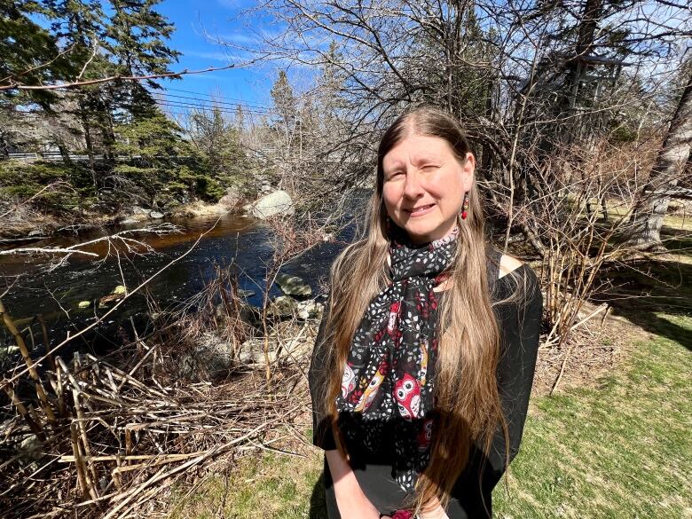 A woman smiles for the camera in an outdoor photo taken with a river in the background.