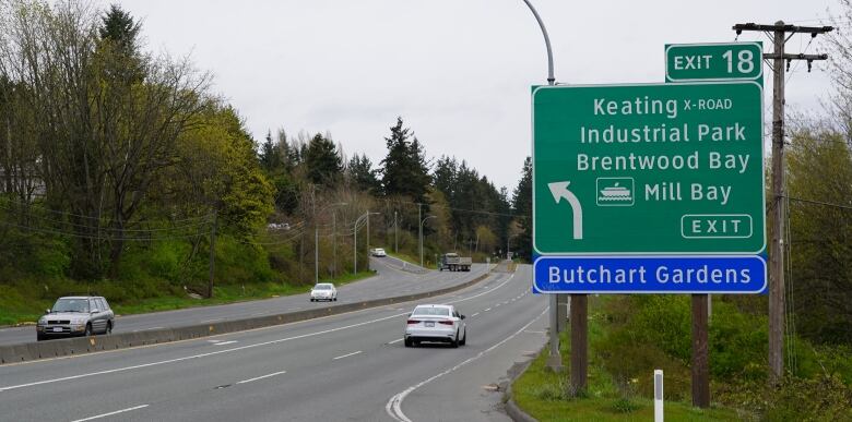 A highway exit sign reads Keating Cross Road Industrial Park, Brentwood Bay, Mill Bay ferry and Butchart Gardens. A truck turns left across traffic. 