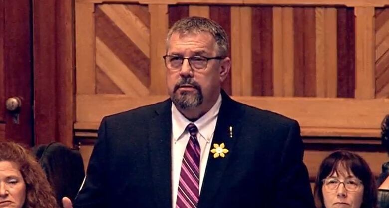 Screen shot of man in a suit speaking at a government gathering. 