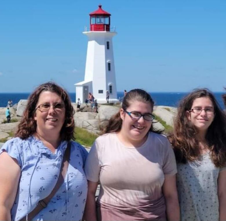 A woman and her two children stand smiling in front of the Peggys Cove lighthouse.