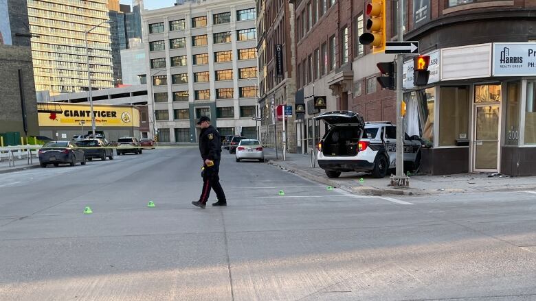 A police officer puts down evidence markers at the scene of a crash, where a police cruiser hit a building at the corner of Notre Dame Avenue and Donald Street.