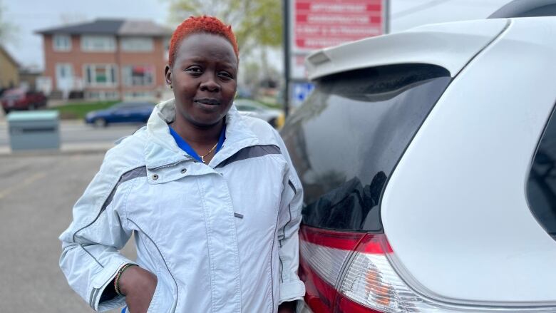 A woman leans against her car and looks into the camera. 