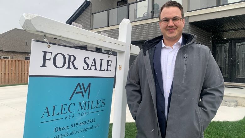 A man stands in front of a home for sale. 