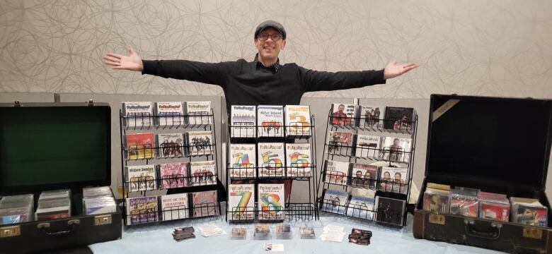 A man stands smiling behind a table covered with cassettes, CDs and DVDs