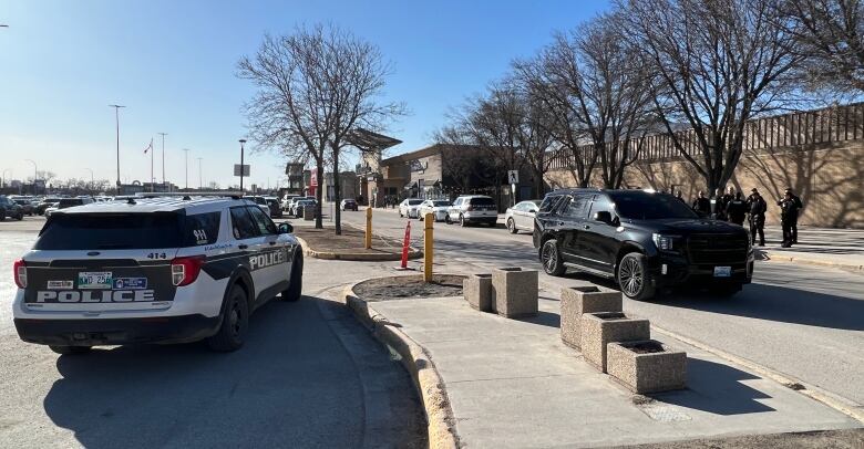 A police vehicle and several officers are seen outside a mall on a sunny day.