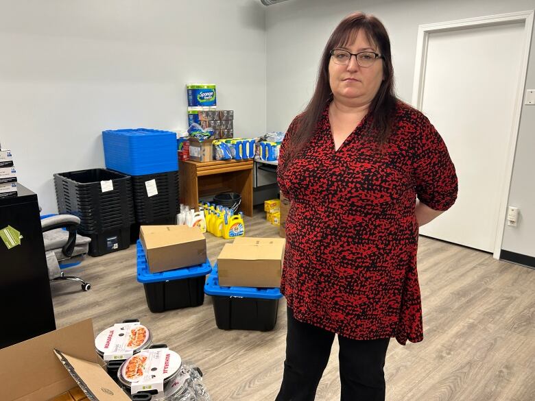 A woman wearing a red a black shirt stands in a room with cleaning supplies in the background.