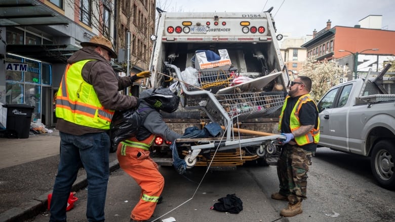 Three men with vests put rubbish and cart into a truck.