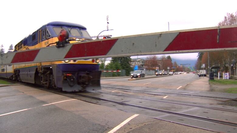 A train crossing arm is down and a West Coast Express train speeds along.