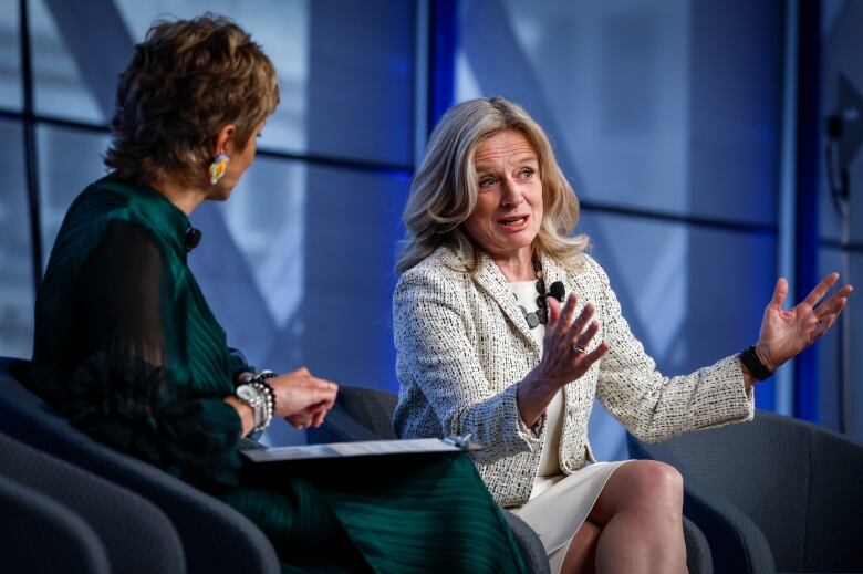 A woman talking while another woman's back is turned to the camera.