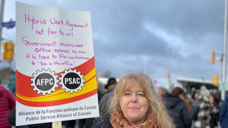 Someone holds a sign at a protest with a long message about the challenges of working in the office.